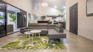 A modern living room with a sectional sofa, a small round table, and a large tropical leaf-patterned rug. - Villa Margarita - Families Getaway in La Fortuna (La Fortuna)