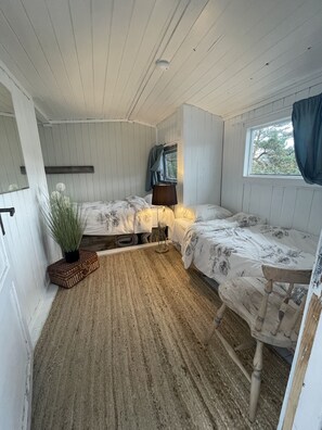 A small, cozy room with two beds, a window with curtains, a bedside lamp, and a potted plant. - Summerhouse with a private beach (Viken)
