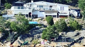 Une grande maison à plusieurs étages, dotée d’un balcon, située sur une côte rocheuse, avec une piscine et des bateaux à proximité.