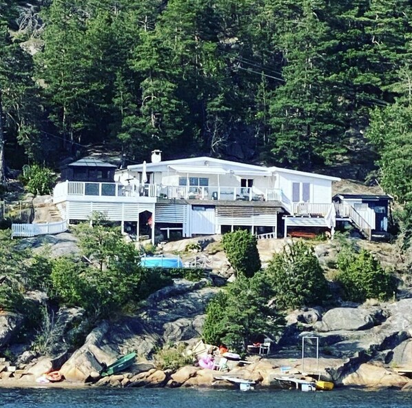 A large, multi-story house with a balcony, situated on a rocky shoreline with a pool and boats nearby. - Summerhouse with a private beach (Viken)