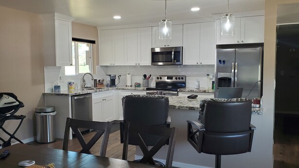 Una cocina moderna con armarios blancos, electrodomésticos de acero inoxidable y un comedor con sillas negras.