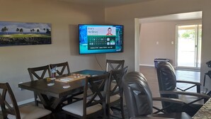 Un comedor con una mesa y sillas, un televisor mostrando a un golfista y un cuadro de un campo de golf.