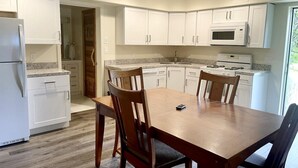 Una cocina moderna con armarios blancos, encimera de granito, mesa de comedor de madera y microondas integrado.