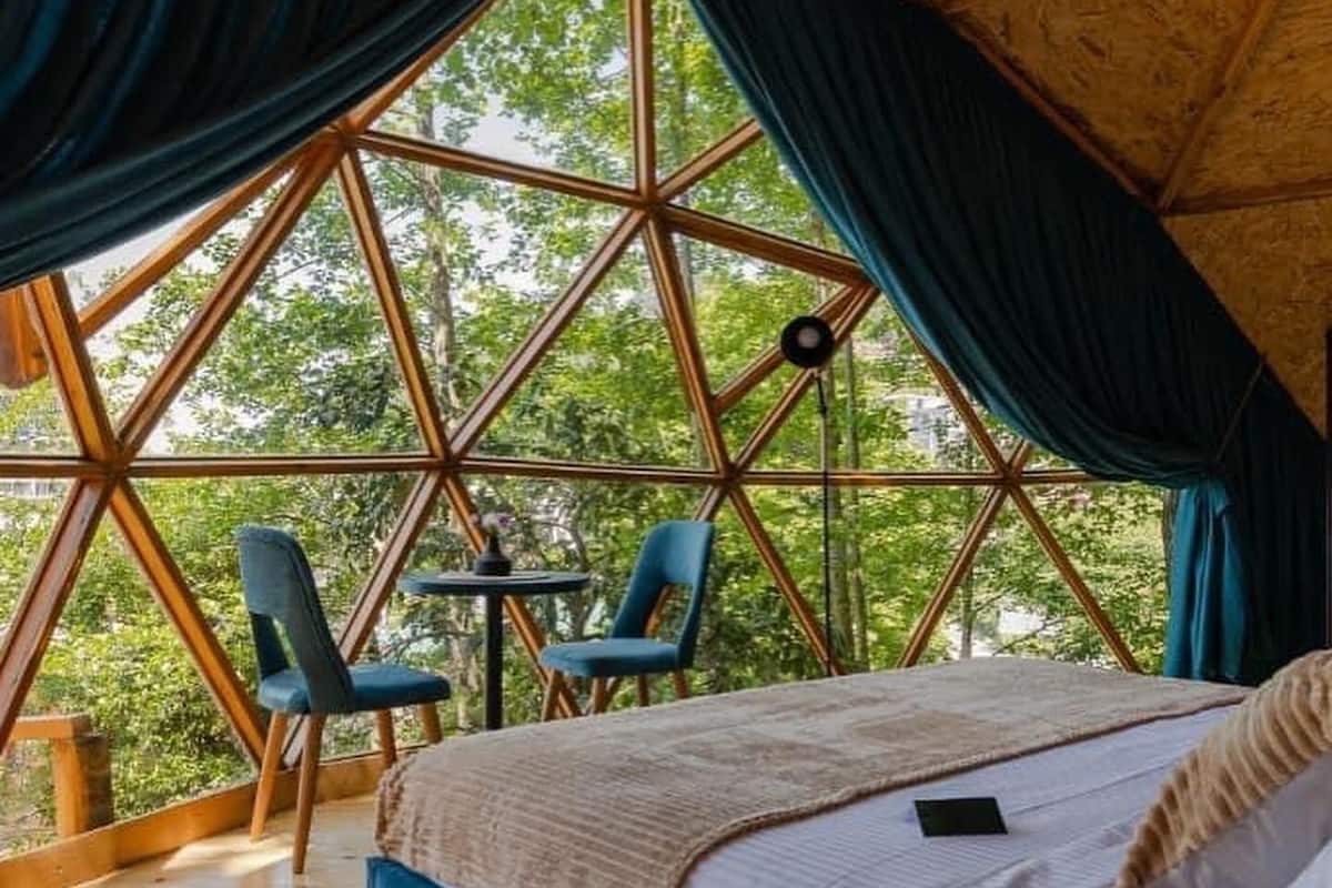 A cozy bedroom with a large window, a bed, and two chairs.