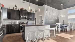A modern kitchen with dark cabinets, stainless steel appliances, and a central island with bar stools. - Nelly: Pet Friendly + Private Hot Tub + Sand Dunes (Hurricane)