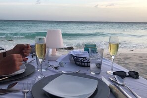A table set for two with a view of the ocean, a bottle of champagne, and a glass of water. - 46 sec to Beach Pool Side Massage Priv Chef UTV (Noord)