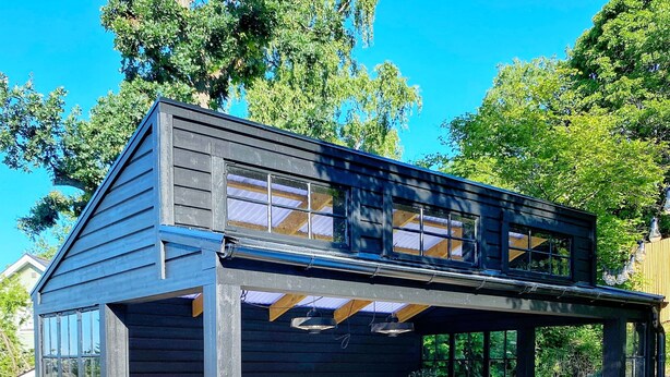 Eine Holzterrasse mit einer Tischtennisplatte, Sitzgelegenheiten im Freien und einem überdachten Bereich mit einer Pergola.