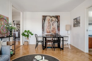 A dining area with a table and chairs, a potted plant, and a large abstract painting on the wall.