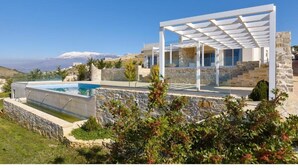 A modern house with a pool, stone walls, and a view of snow-capped mountains. - Elkysti Crete Superior Apartment "Nikos" (Kreta)