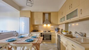 A modern kitchen with wooden cabinets, a built-in oven, and a dining area with a table set for four. - Elkysti Crete Superior Apartment "Nikos" (Kreta)