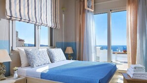 Een hotelkamer met een groot bed, uitzicht op zee en een balkon met een tafel en stoelen.