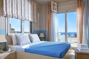 Une chambre d’hôtel avec un grand lit, une vue sur la mer et un balcon équipé d’une table et de chaises.