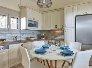 A modern kitchen with white cabinets, a stainless steel refrigerator, and a round dining table set with blue plates and glasses. - Elkysti Crete Deluxe Apartment "Eleftheria" (Kreta)