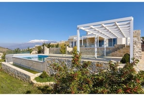 A modern house with a pool, stone walls, and a view of snow-capped mountains. - Elkysti Crete Deluxe Apartment "Eleftheria" (Kreta)