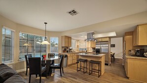 A modern kitchen with wooden cabinets, a central island, and a dining area with a table and chairs. - Warm 4BR W/ Loft home, 15min to strip, Near Summerlin! Pool & Spa! Pet Friendly! (Las Vegas)