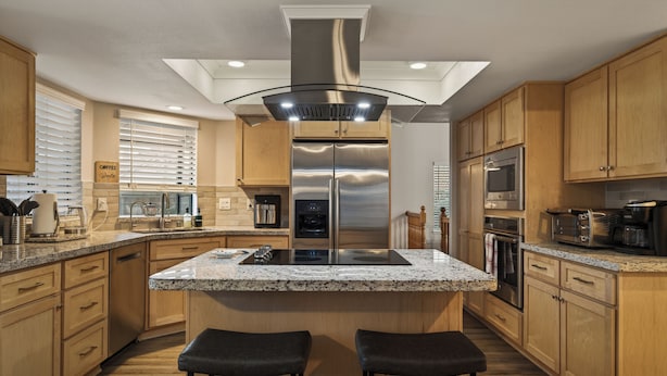 A modern kitchen with a central island, stainless steel appliances, wooden cabinets, and a large window with blinds. - Warm 4BR W/ Loft home, 15min to strip, Near Summerlin! Pool & Spa! Pet Friendly! (Las Vegas)