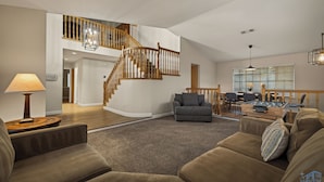 A spacious living area with a curved staircase, a sofa set, a coffee table, and a dining area with a table and chairs. - Warm 4BR W/ Loft home, 15min to strip, Near Summerlin! Pool & Spa! Pet Friendly! (Las Vegas)