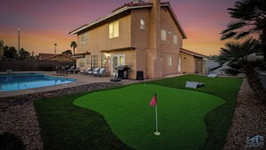 A two-story house with a swimming pool, a well-maintained lawn, and a patio area with outdoor furniture. - Warm 4BR W/ Loft home, 15min to strip, Near Summerlin! Pool & Spa! Pet Friendly! (Las Vegas)