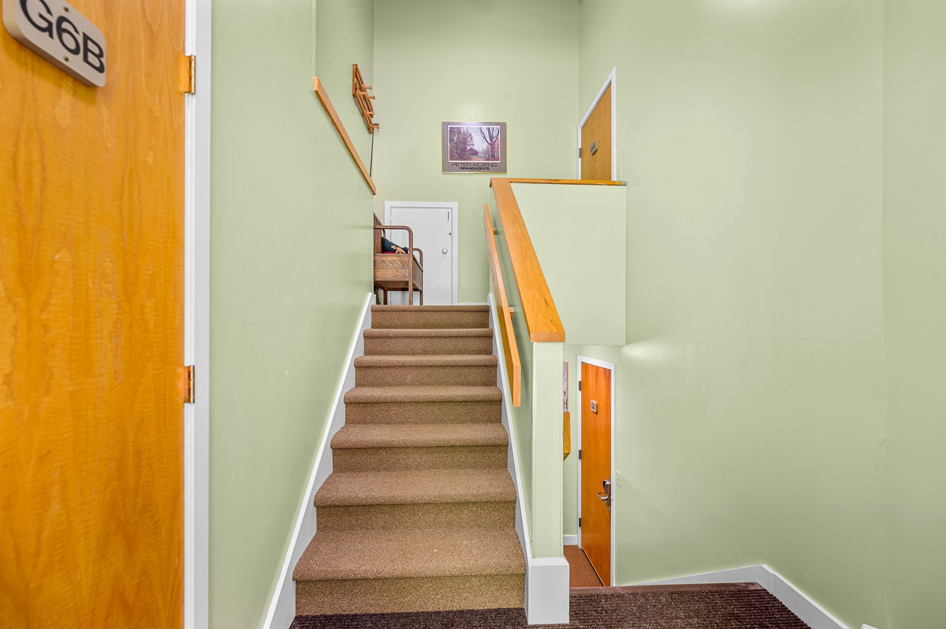 A carpeted staircase with a wooden handrail and a door labeled "G6B" on the left.