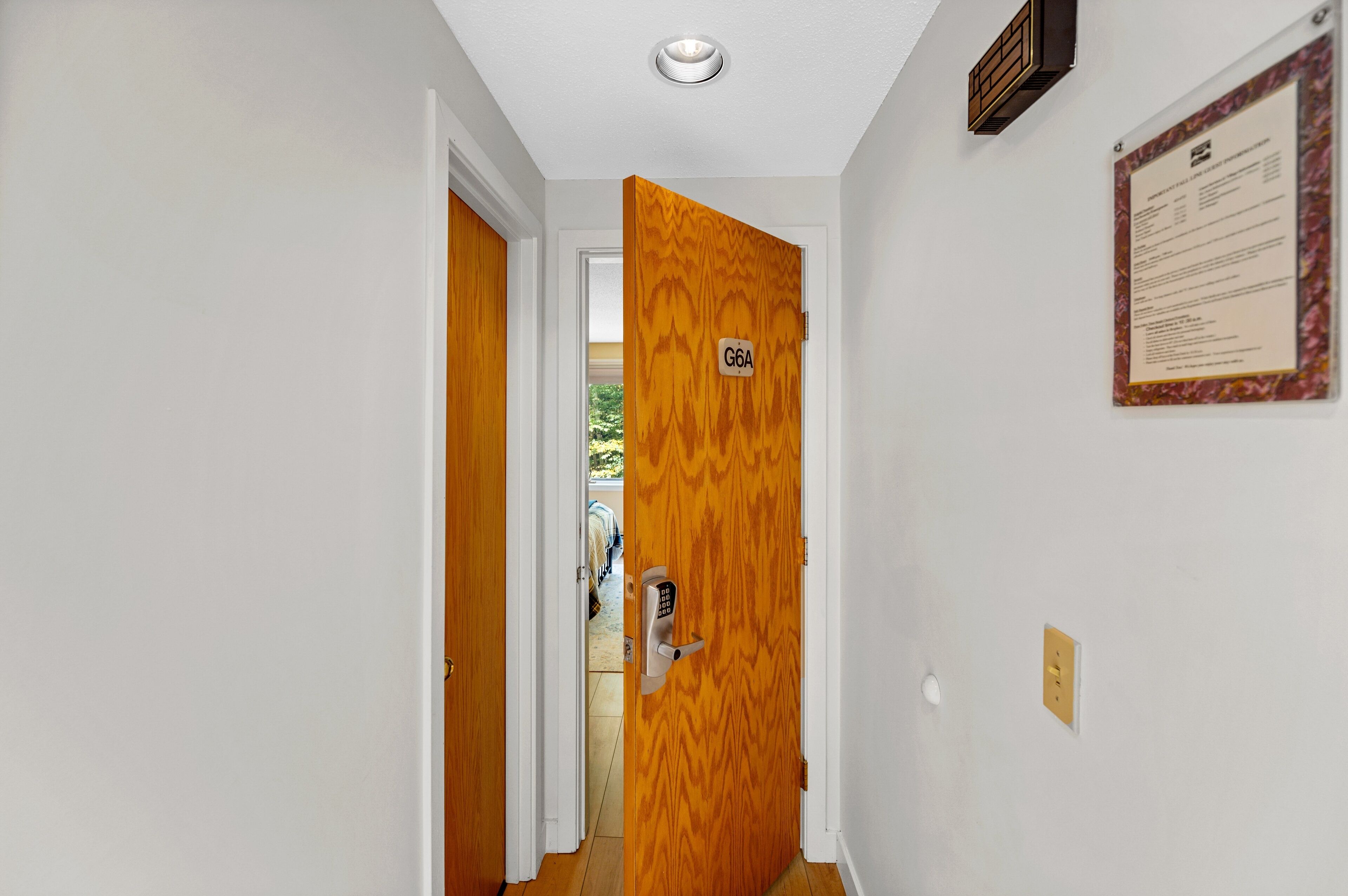 A hallway with a wooden door labeled G6A, a wall-mounted light switch, and a bulletin board with text.