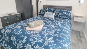Une chambre à coucher comprenant un lit, une table de chevet, une commode, un miroir et un luminaire fixé au mur.