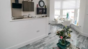 Une cuisine moderne avec des meubles blancs, une horloge et un coin repas comprenant une table et des chaises.