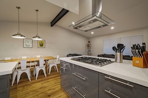 Cozinha moderna com ilha central, cadeiras brancas, luminárias pendentes e coifa de aço inoxidável.