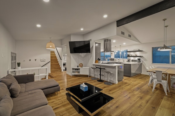 A modern living space with a sofa, a coffee table, a kitchen area, and a dining table.