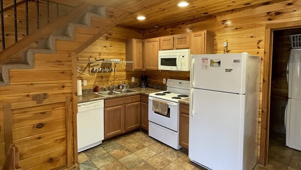 A wooden cabin kitchen with a stove, microwave, and refrigerator.