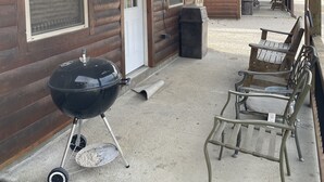 A wooden cabin with a covered porch, a barbecue grill, and outdoor seating.