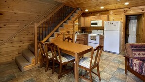 A wooden interior with a dining table and chairs, a kitchen area with appliances, and a staircase.
