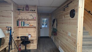 A wooden-paneled room with a desk, chair, shelves with books, a lantern, and fishing equipment.