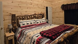 A wooden cabin-style bedroom with a bed, a nightstand, a lamp, and a ceiling fan.