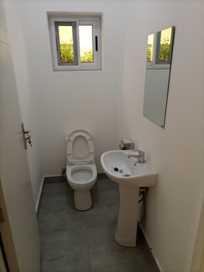 A small, clean bathroom with a toilet, sink, and a window above the toilet.