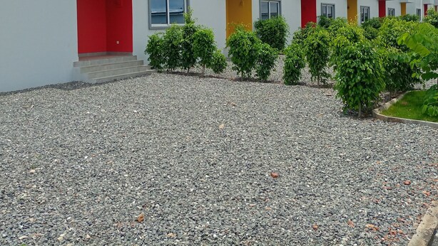 Een modern gebouw met een reeks ramen en deuren, een grindpad en kleine groene struiken.