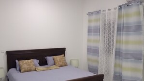 Een slaapkamer met een houten bed, een nachtkastje, een lamp en een raam met gordijnen.