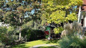 Ein Garten mit einem gewundenen Pfad, einem kleinen Spielhäuschen und einem Haus mit rotem Dach.