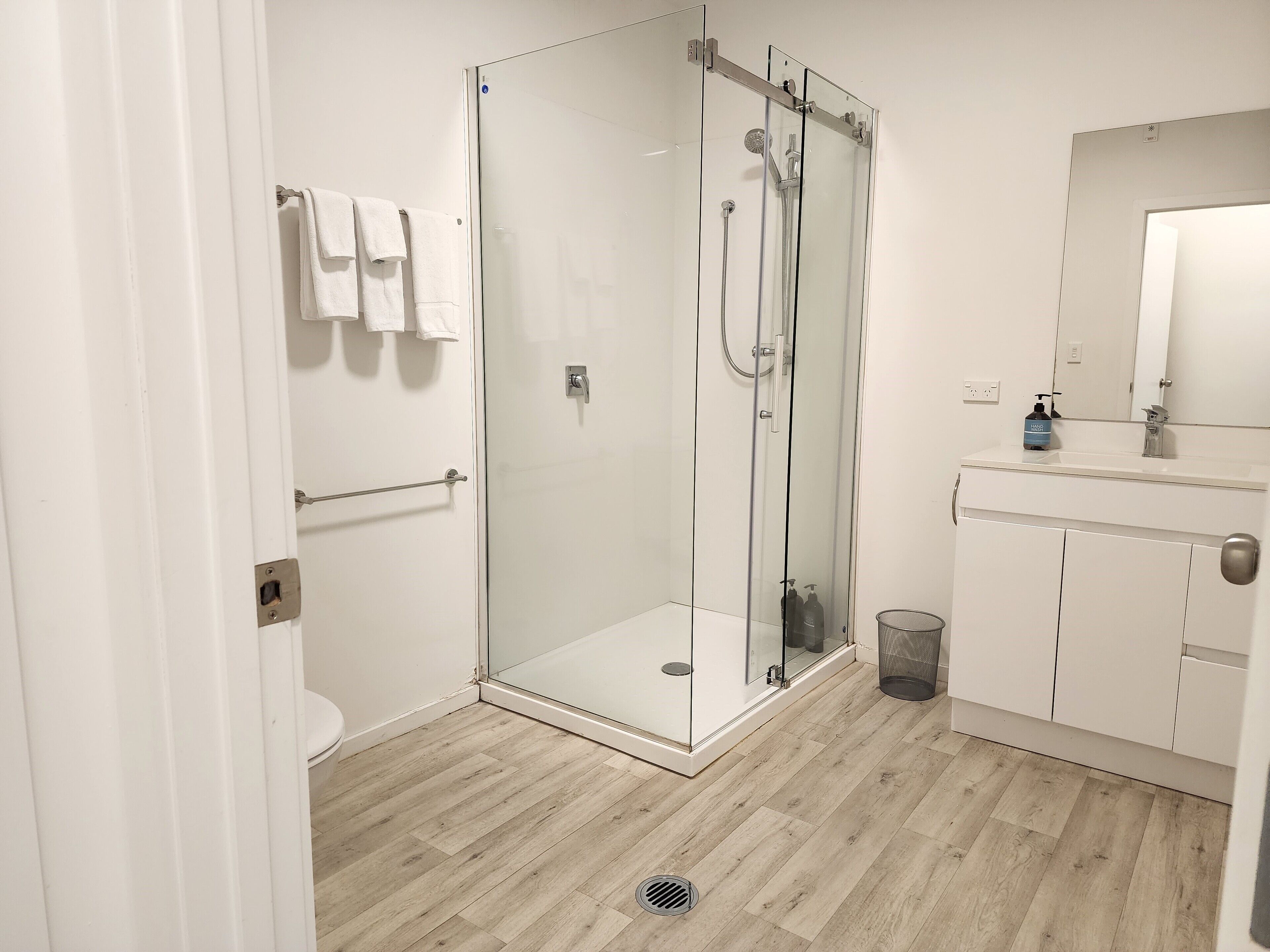 A modern bathroom with a glass-enclosed shower, a toilet, a sink with a mirror, and a towel rack.