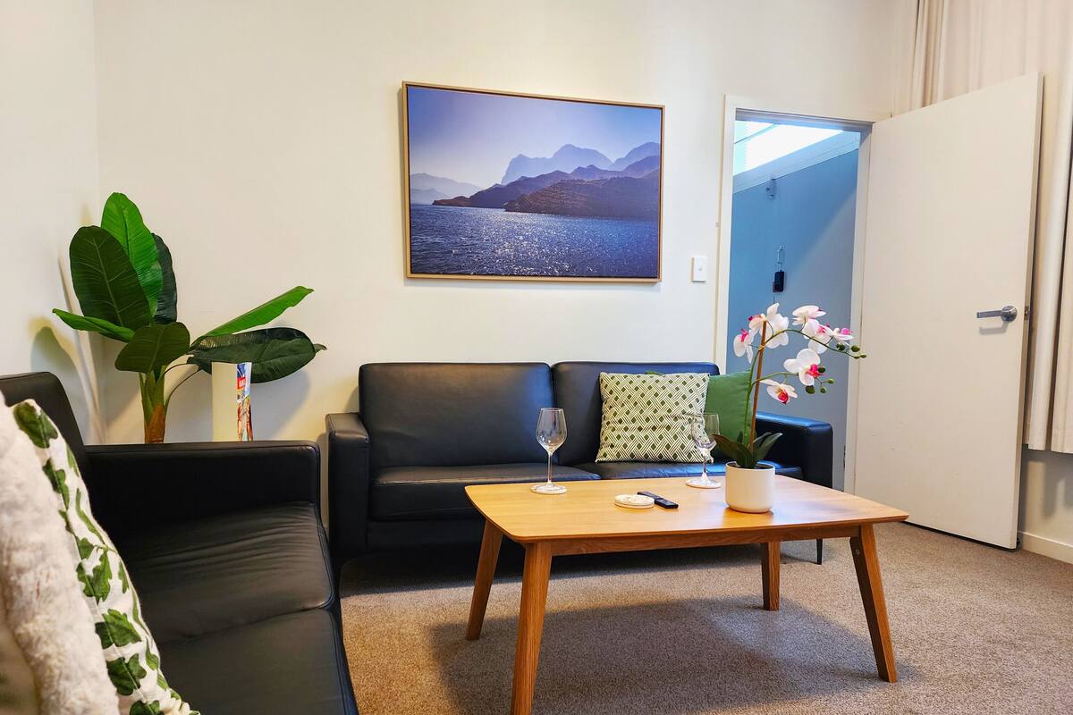 A living room with a black leather sofa, a wooden coffee table, and a large framed picture on the wall.