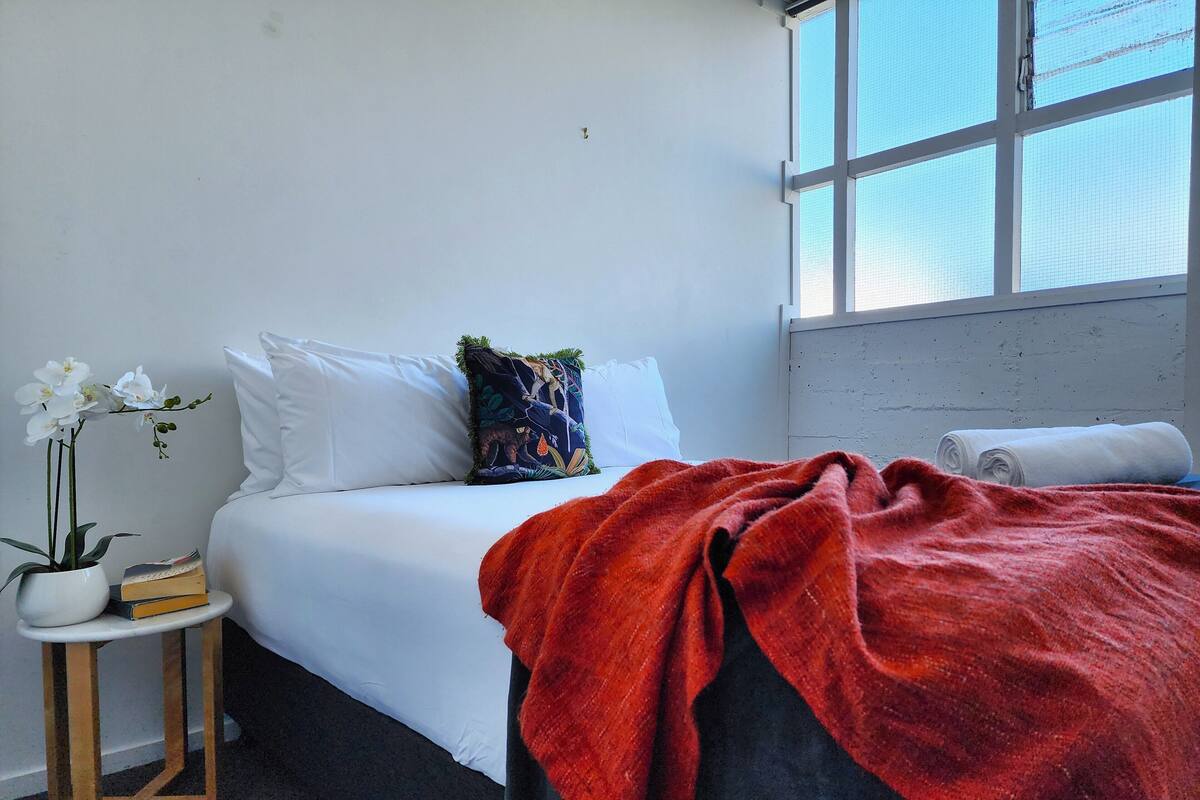 A bedroom with a bed, a small side table, a window, and a red blanket.