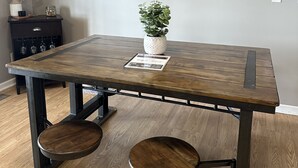 Uma mesa de jantar com um relógio na parede, uma planta em vaso e uma pequena placa.