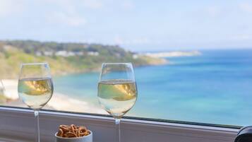Two glasses of white wine on a windowsill with a bowl of pretzels, overlooking a coastal view.