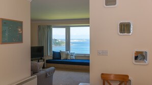 Une chambre avec vue sur la mer, une télévision, une table à manger avec des chaises et une fenêtre avec des rideaux.