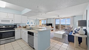 Een moderne keuken met een centraal kookeiland, een eethoek met uitzicht en een woonkamer met balkon over de zee.