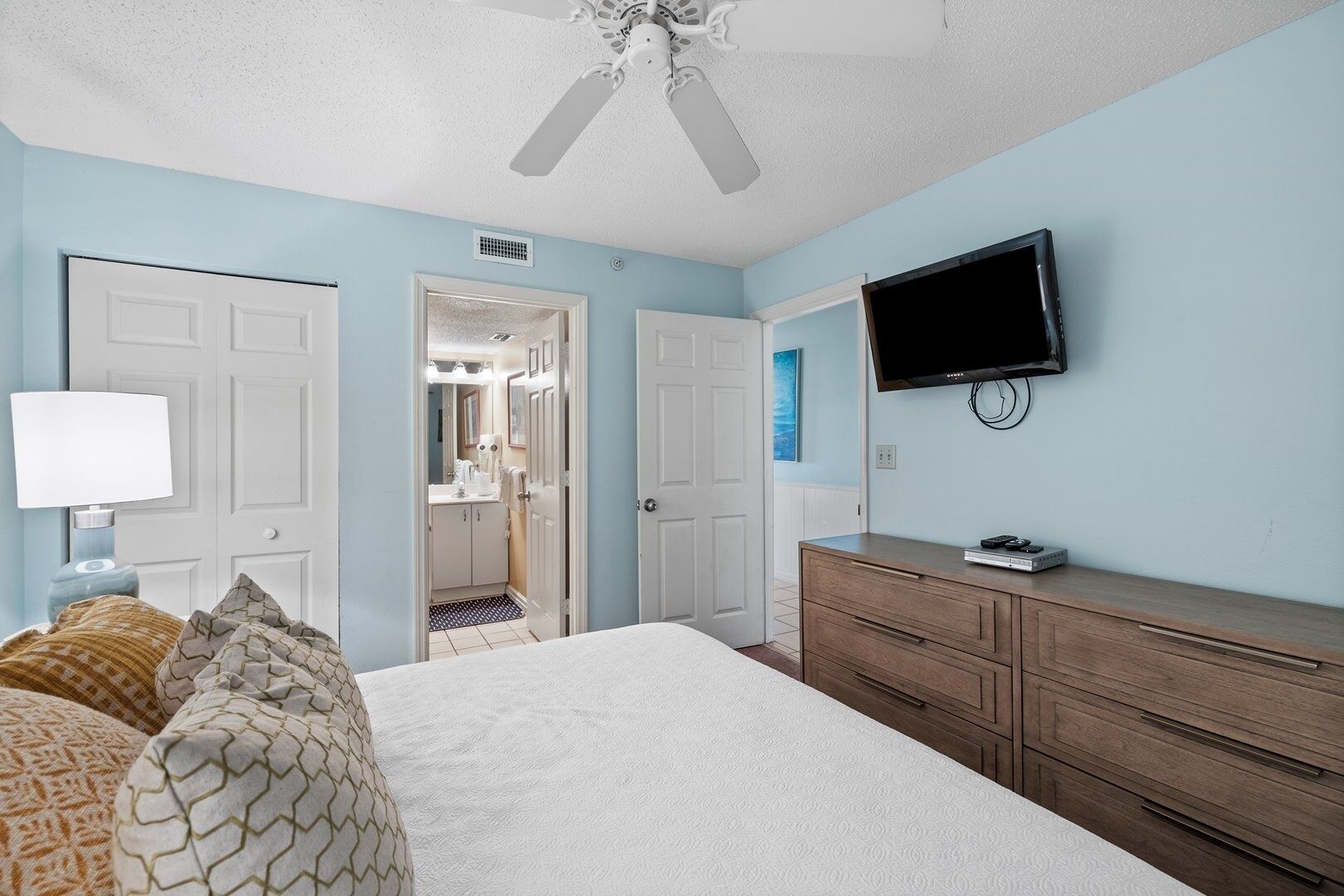 A bedroom with a bed, a dresser, a TV, and a ceiling fan.
