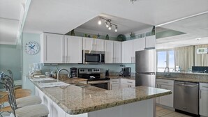 A modern kitchen with white cabinets, a granite countertop, stainless steel appliances, and a breakfast bar. - Pelican Beach 1510 1 Bedroom Condo by Pelican Beach Management (Destin)