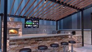 An outdoor bar area with a stone counter, bar stools, a television screen, and a wood-paneled ceiling.