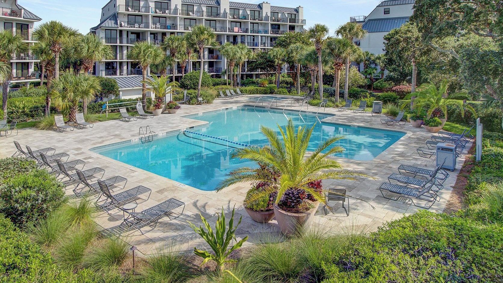A hotel pool area with a rectangular pool, lounge chairs, and palm trees.