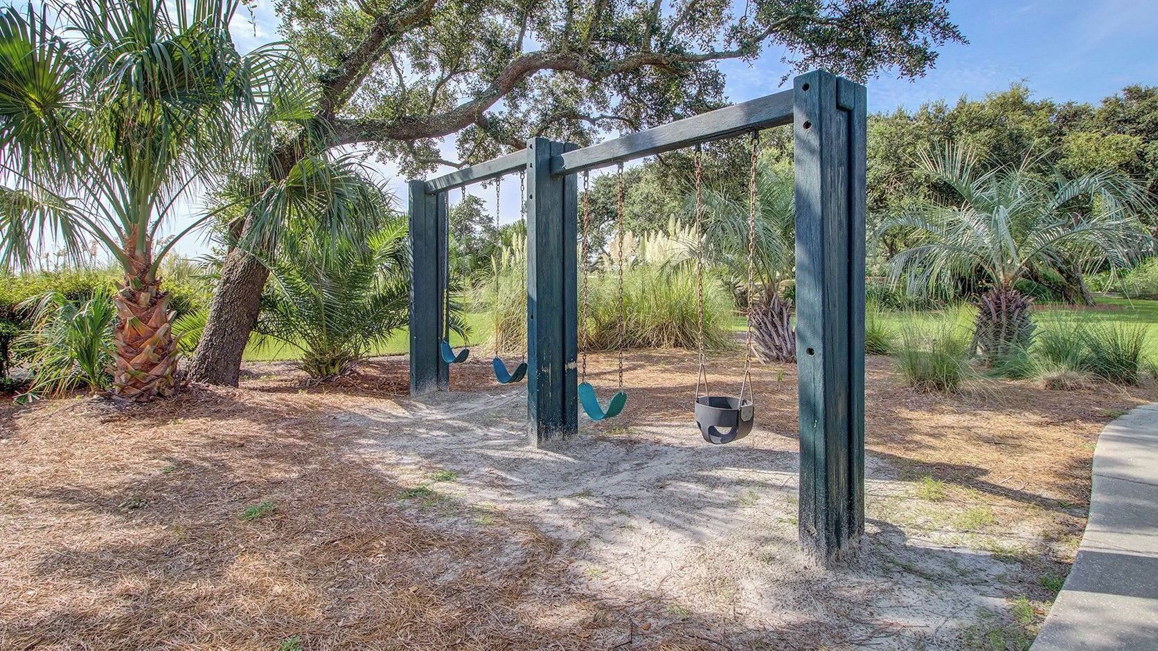 A swing set in a park with trees and shrubs.