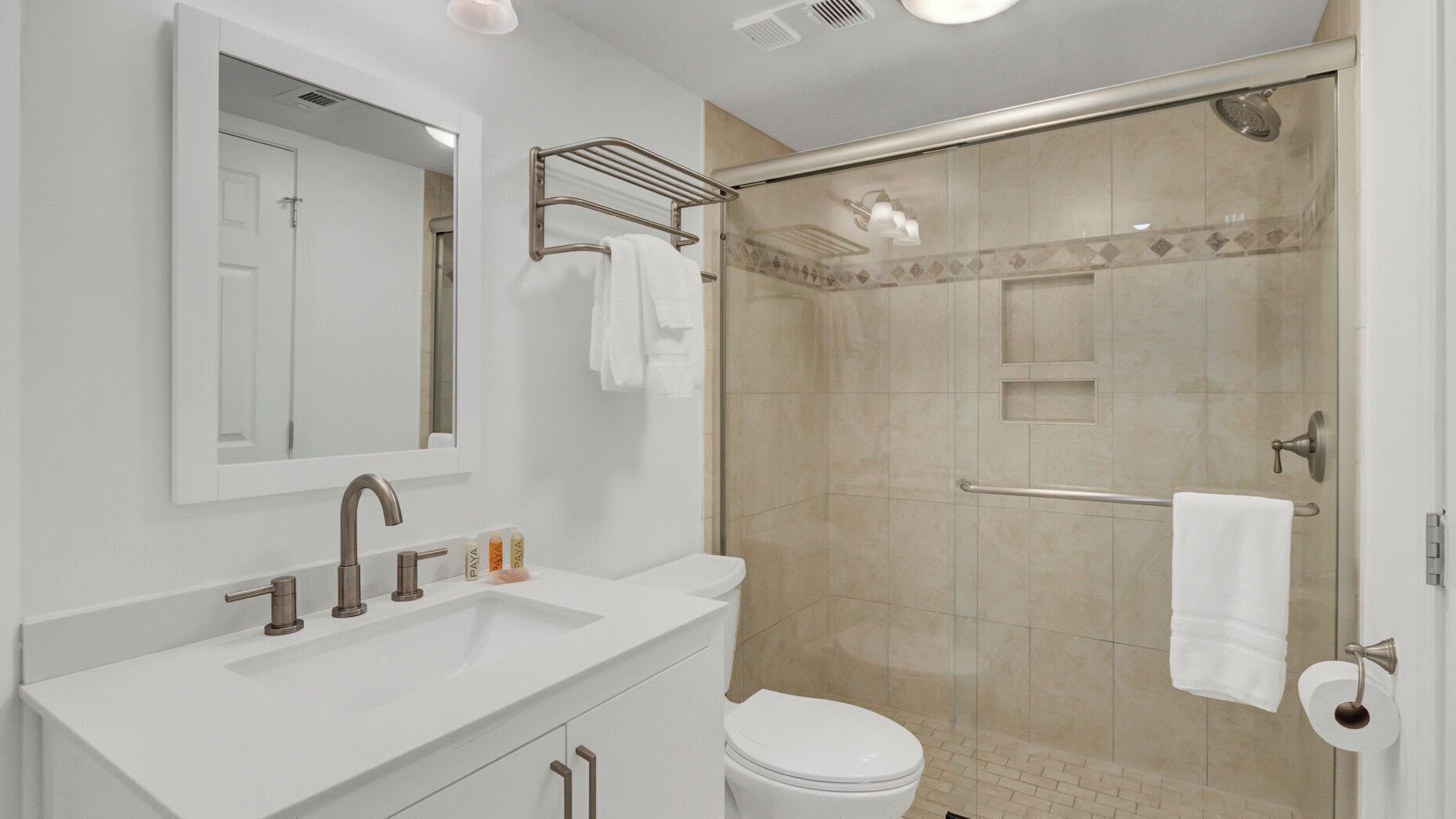 A modern bathroom with a white sink, a mirror, a toilet, and a glass-enclosed shower.
